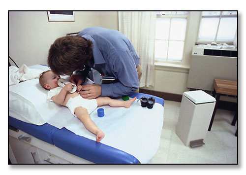Fourth year medical student, Peter Thompson, examines curious and cooperative baby girl. <br>The Family Care Facility, Memorial Hospital, Pawtucket, Rhode Island. January 1984.